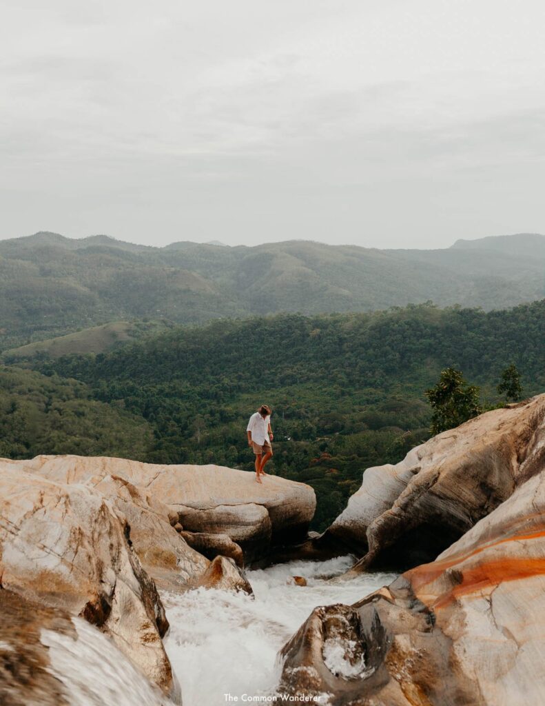 A traveller standing next to the water stream under the rocks from the waterfall.