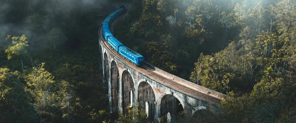 Aerial view of the Nine Arches Bridge with a blue train going through the bridge out side of the city of Ella.