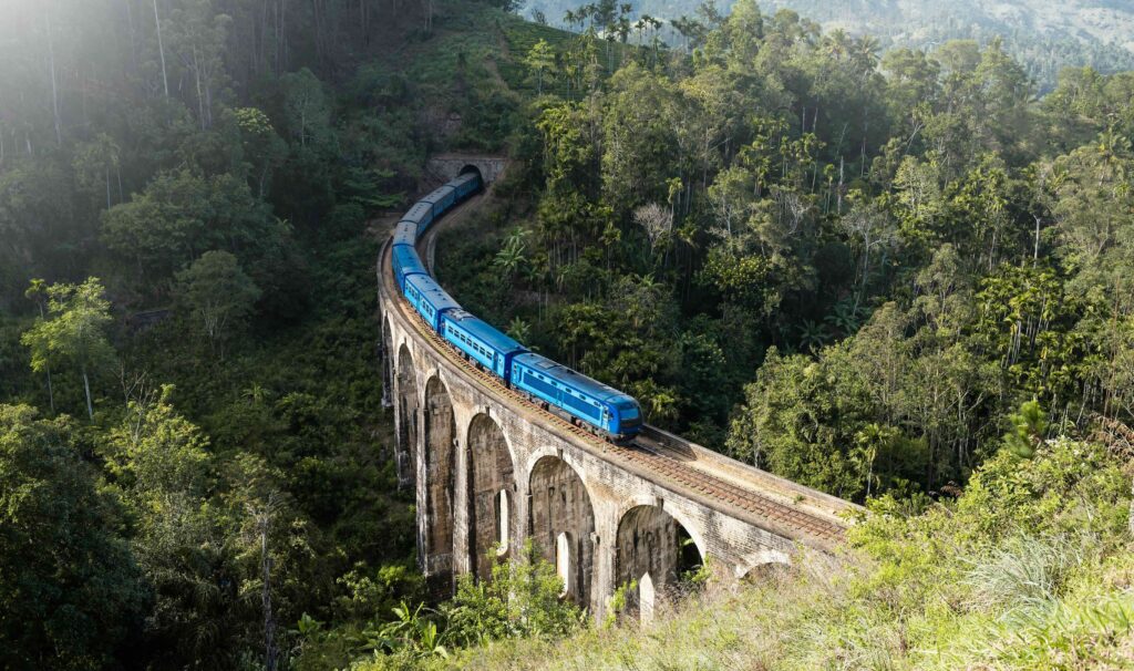 Aerial view of a blue train crossing a bridge through the forest from Colombo to Kandy.