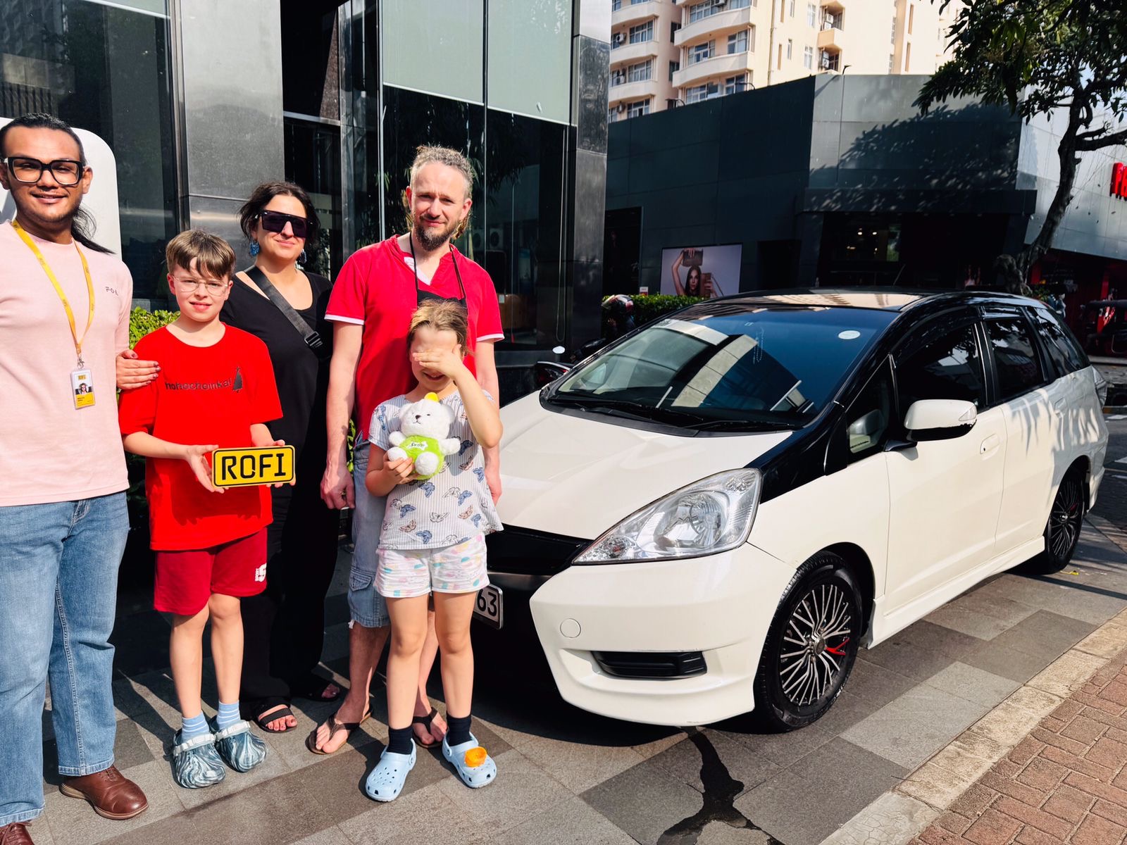 Happy customers accompanied by Rofi team and Rofi vehicle host in front of a black and white two-toned Honda Insight.